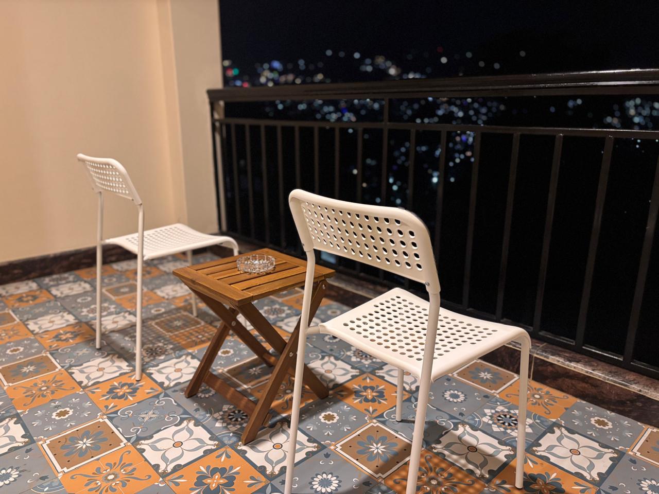 Balcony chairs and a table at night, with the lights of Darjeeling scattered in the darkness below