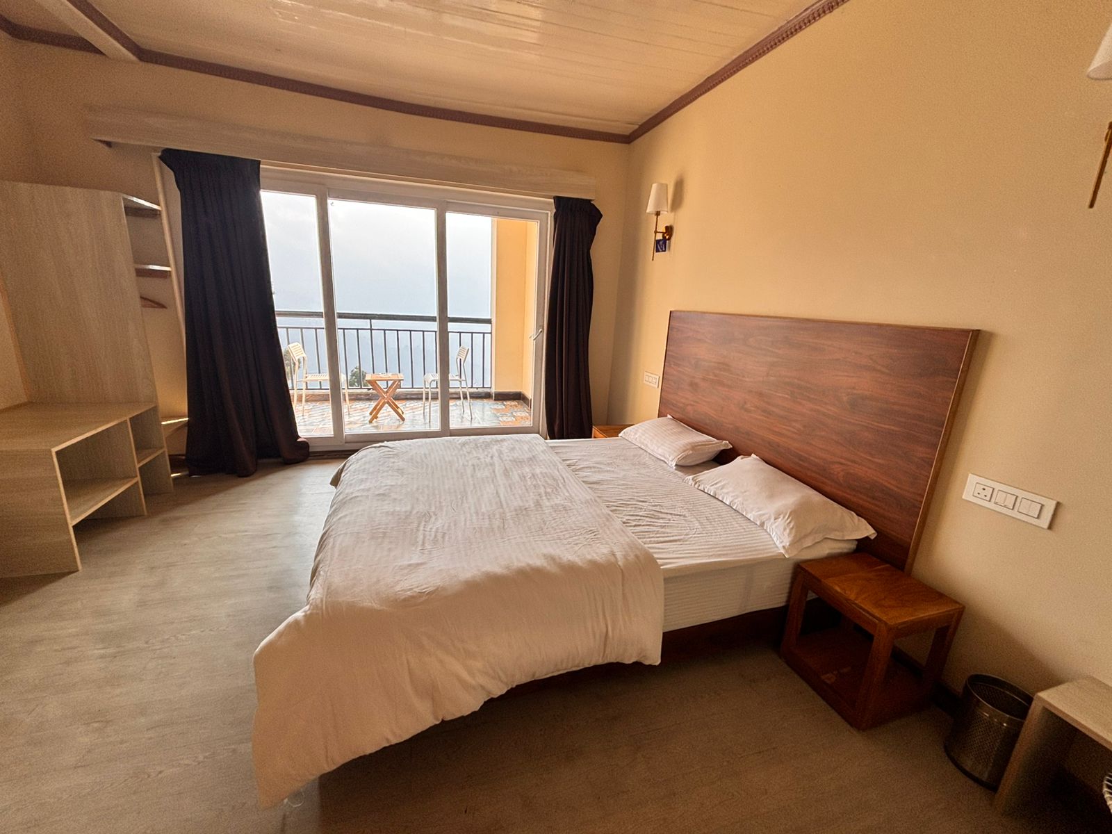 A guest room at Asraya with a dark wooden headboard, white bedding and sliding doors opening onto the balcony