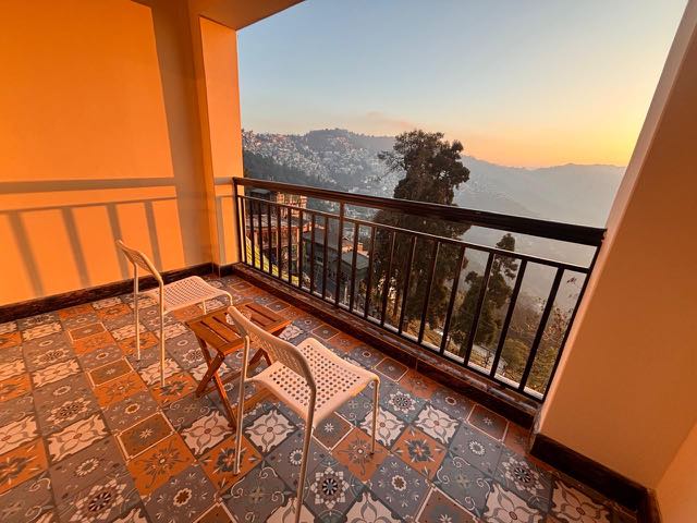 Two chairs and a folding table on an Asraya balcony at golden hour, above Darjeeling town